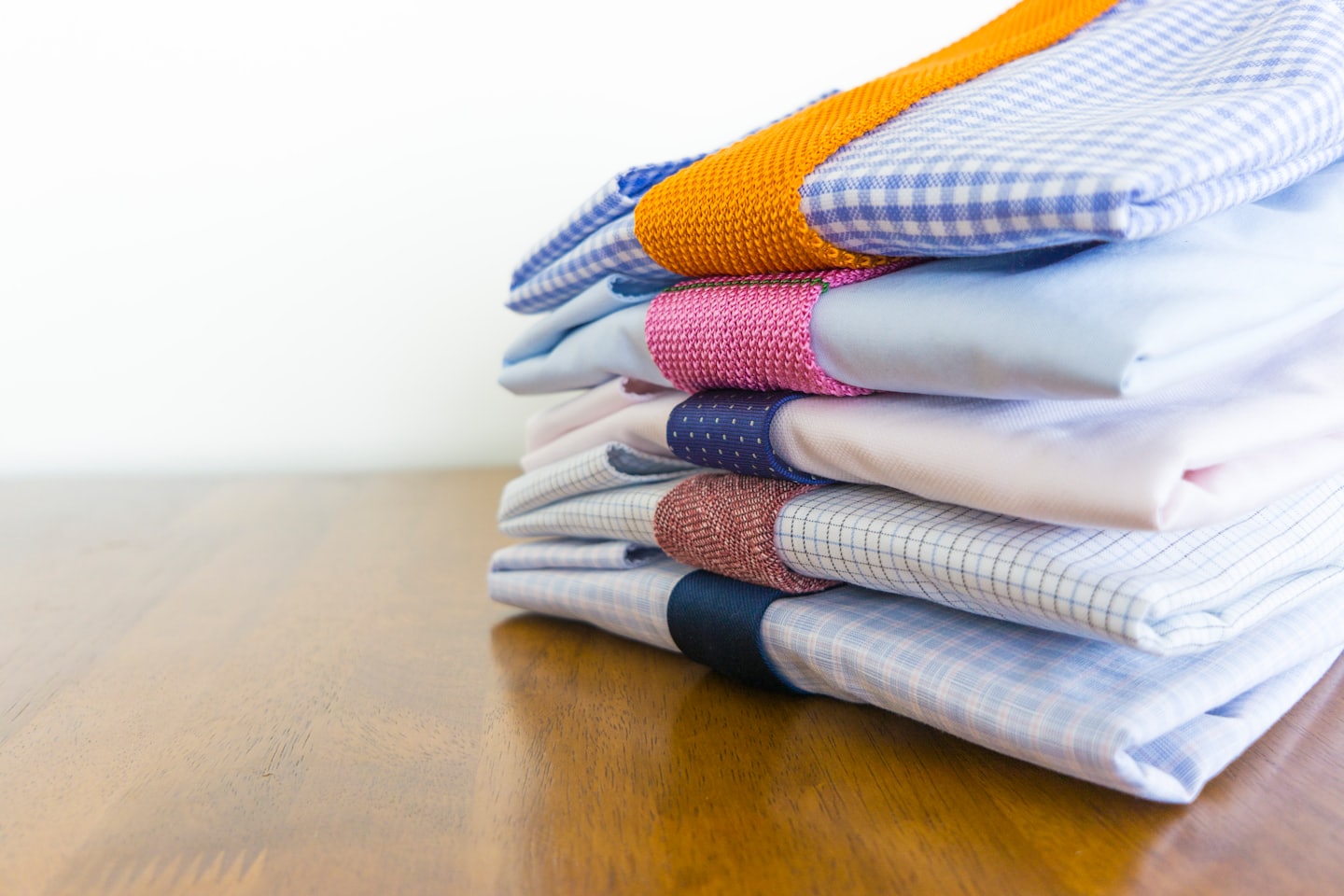 Cinco camisas de vestir dobladas y apiladas sobre una superficie de madera.